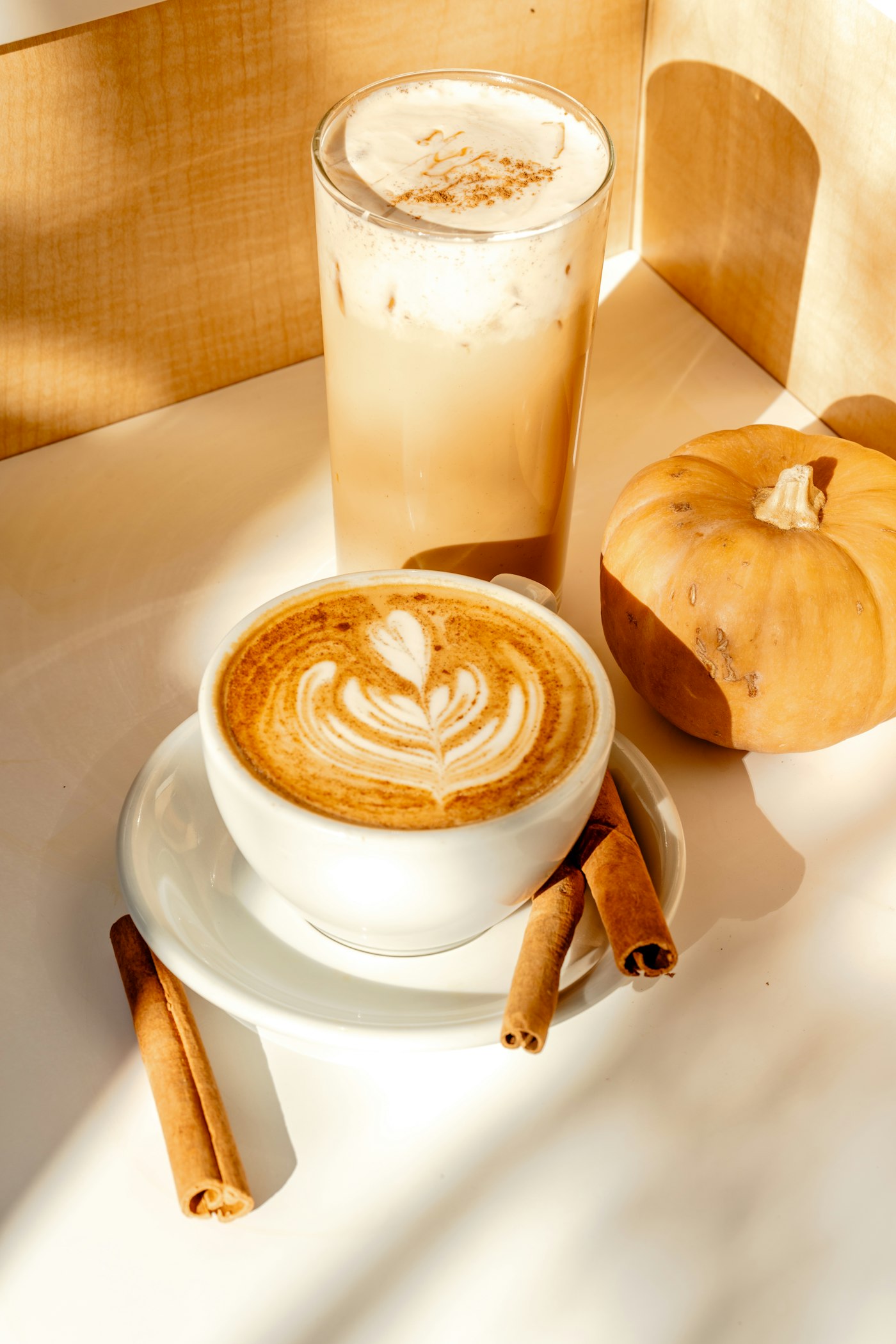 Latte with leaf latte art beside small pumpkins and cinnamon sticks